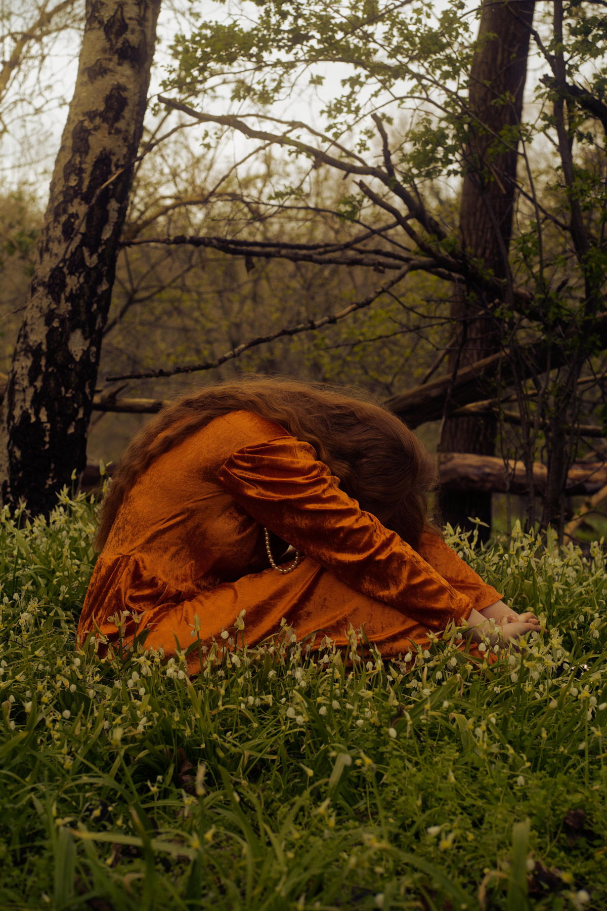 Junge Frau in einem roten Kleid sitzt in einer Waldlichtung. Fotograf: Lea Kutschke, Geraldine Kutschke / TWIINZ.